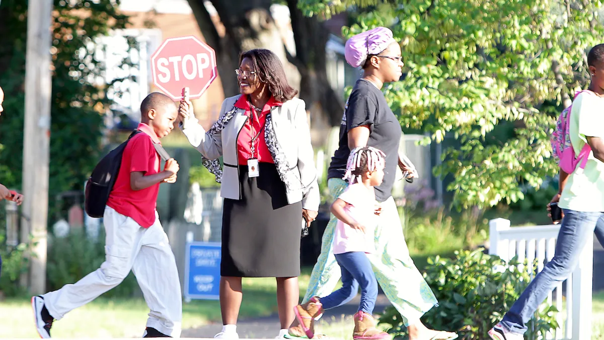 Topeka Public Schools Superintendent Tiffany Anderson stands in a crosswalk with a stop sign as students pass by on their way to school.