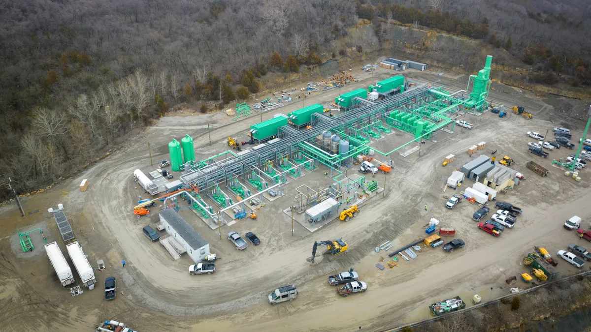 Aerial view of small industrial facility with network of pipes and tanks criss-crossing site surrounded by trees.