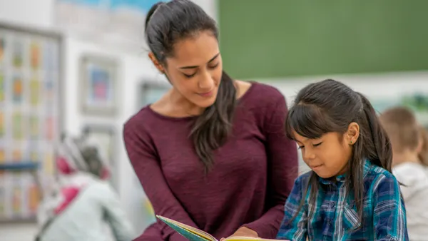 A woman teacher instructs a girl elementary student in reading.