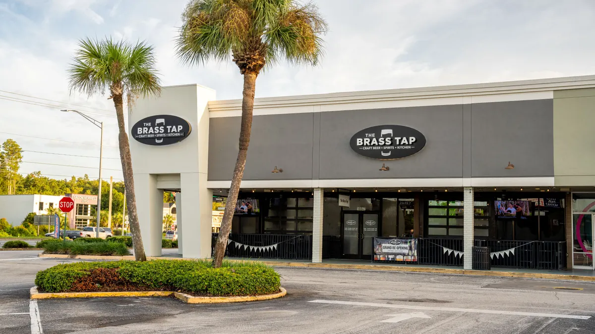 A white resturant with a patio with black trim. There is a logo that says Brass Tap