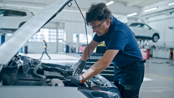 Male mechanic works on a car engine at an auto repair shop.