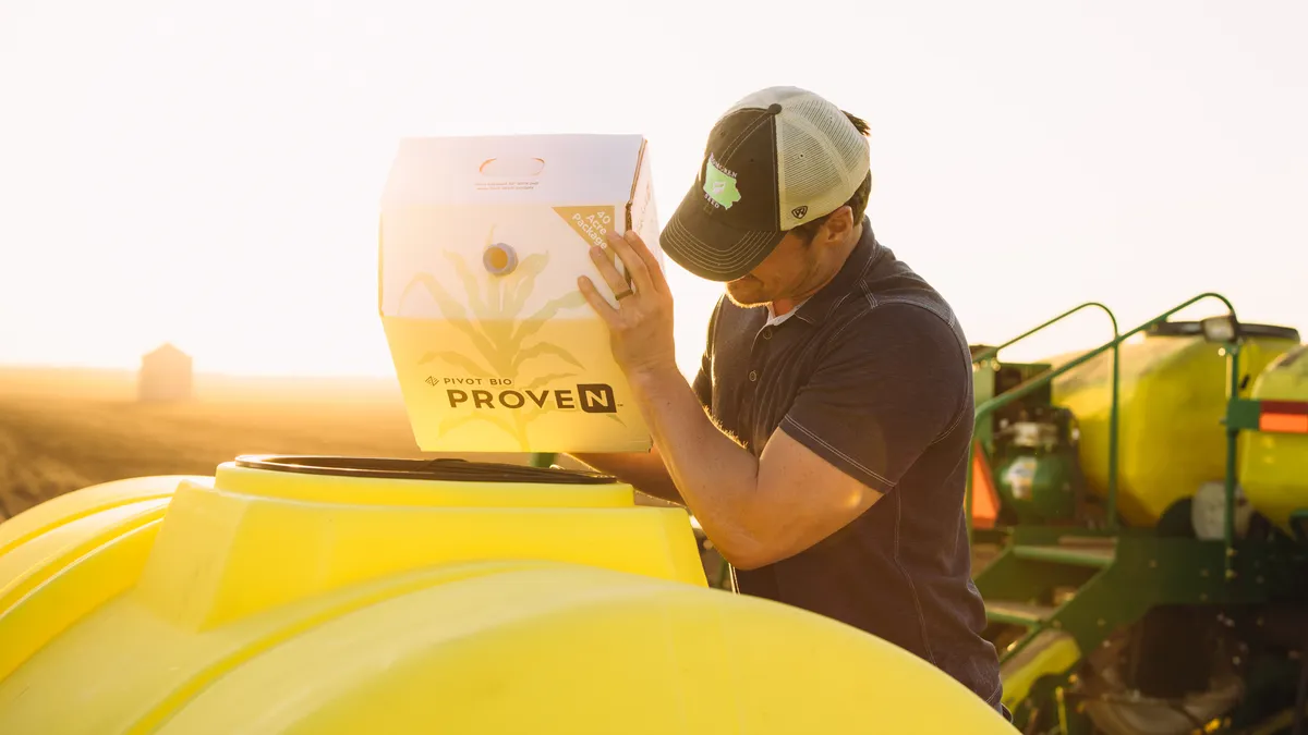 A man in a trucker hat holds a bag of Pivot Bio Product that he pours into equipment.