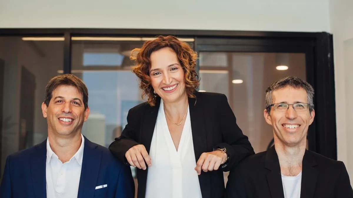 Two men sitting and a woman standing between them.