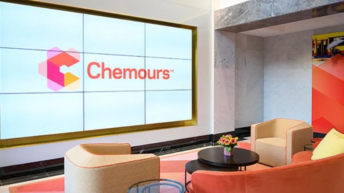 A white screen with The Chemours Co. logo on it, and three light and dark orange chairs in front of it.