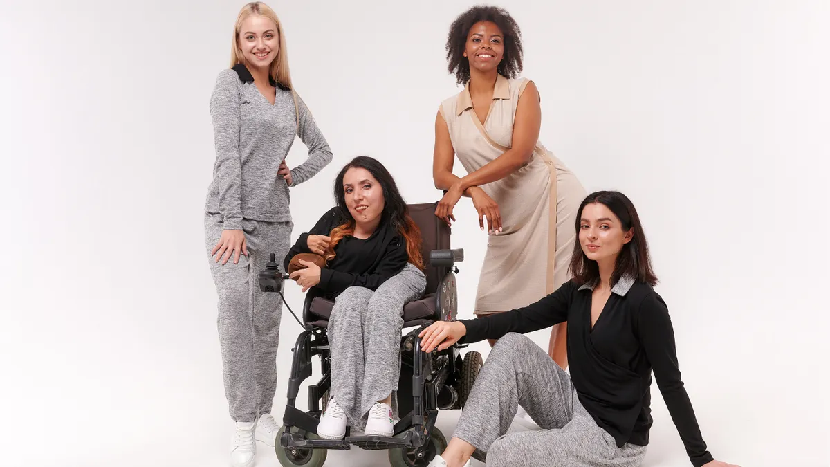 A diverse group of people, one in a wheelchair, all wearing casual clothing in neutral colors.