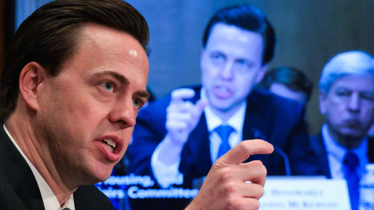 Jonathan McKernan speaks and gestures during a Congressional hearing. A screen in the background also shows him speaking.