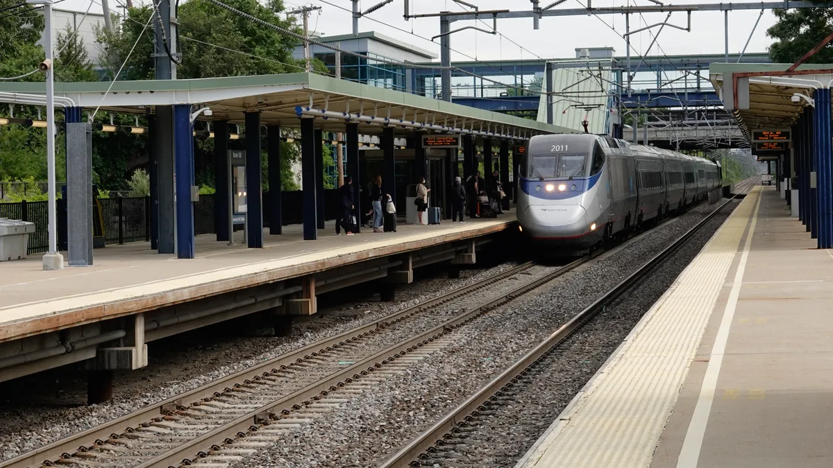 An Amtrak Acela train at a station with waiting passengers.