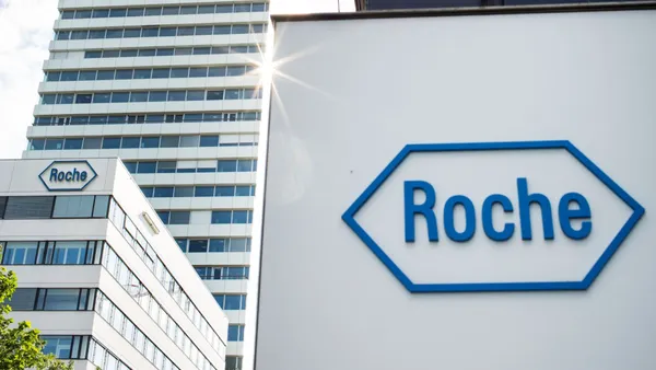 A sign with the Roche logo stands in front of a tall building.