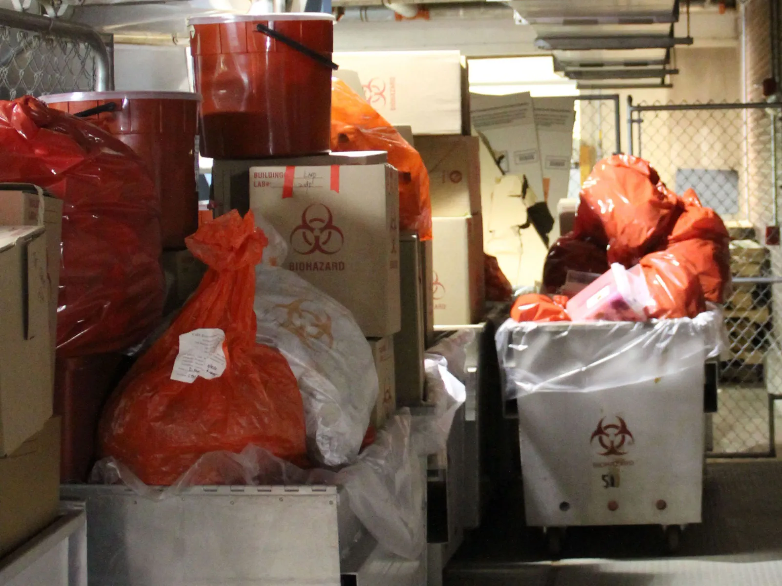 Bags, boxes and bins labeled with the words “Biohazard” and the hazardous waste symbol sit in a storage bay.