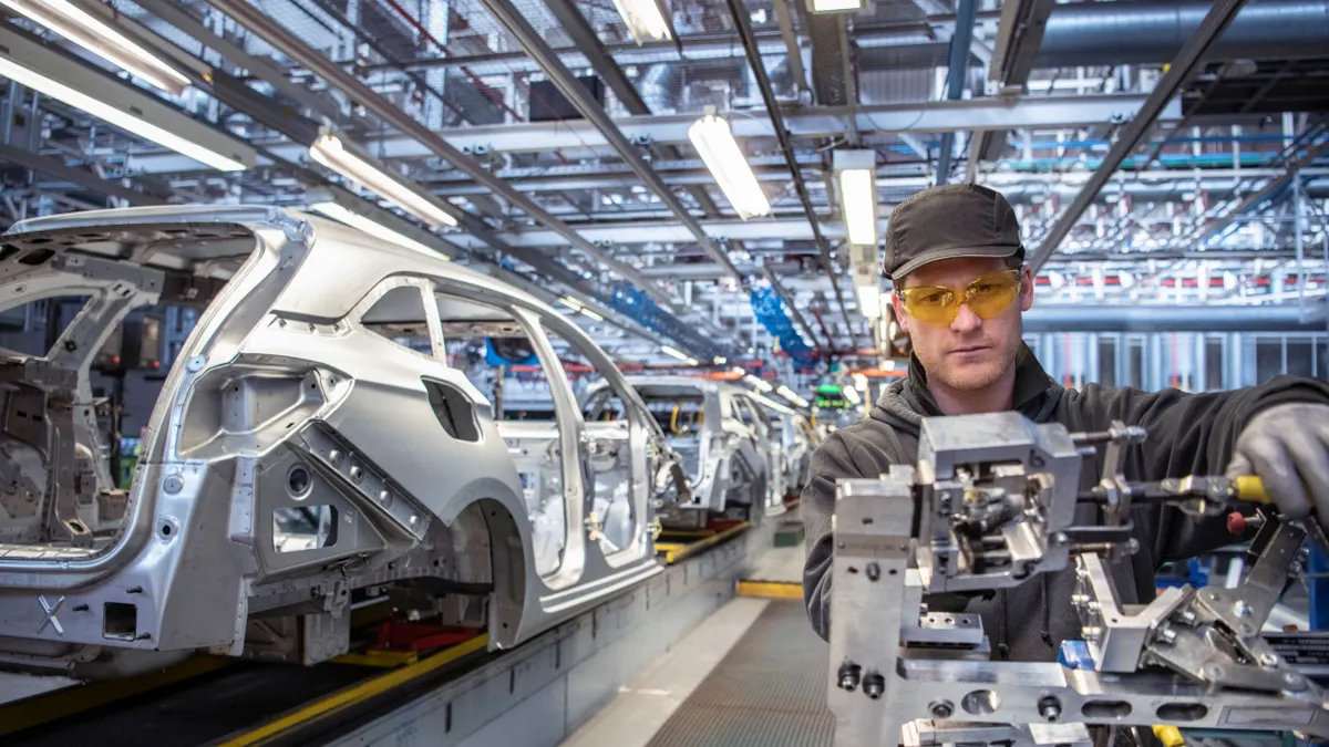 A man in a gray cap and jacket and yellow safety goggles working on a automotive component.