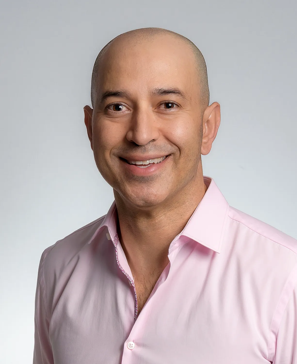 A person in a pink button-up shirt smiles at the camera in a corporate headshot.