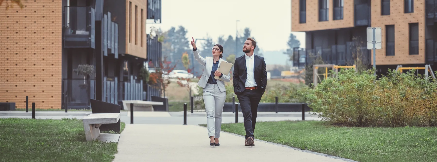 Real estate agent and customer walking between apartment buildings.