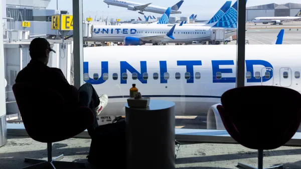 A man sits in an airport with United Airlines aircraft seen in the window behind him.