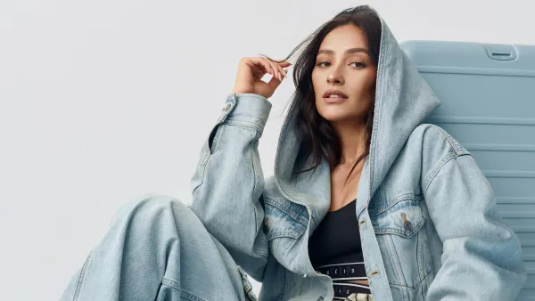 A model wears clothing from the Gap/Beis collection in front of luggage from the collection.