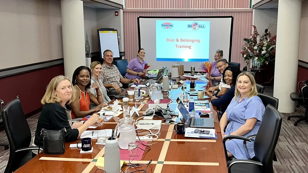 A group of people sit at a table in an office conference room and smile, facing the camera.