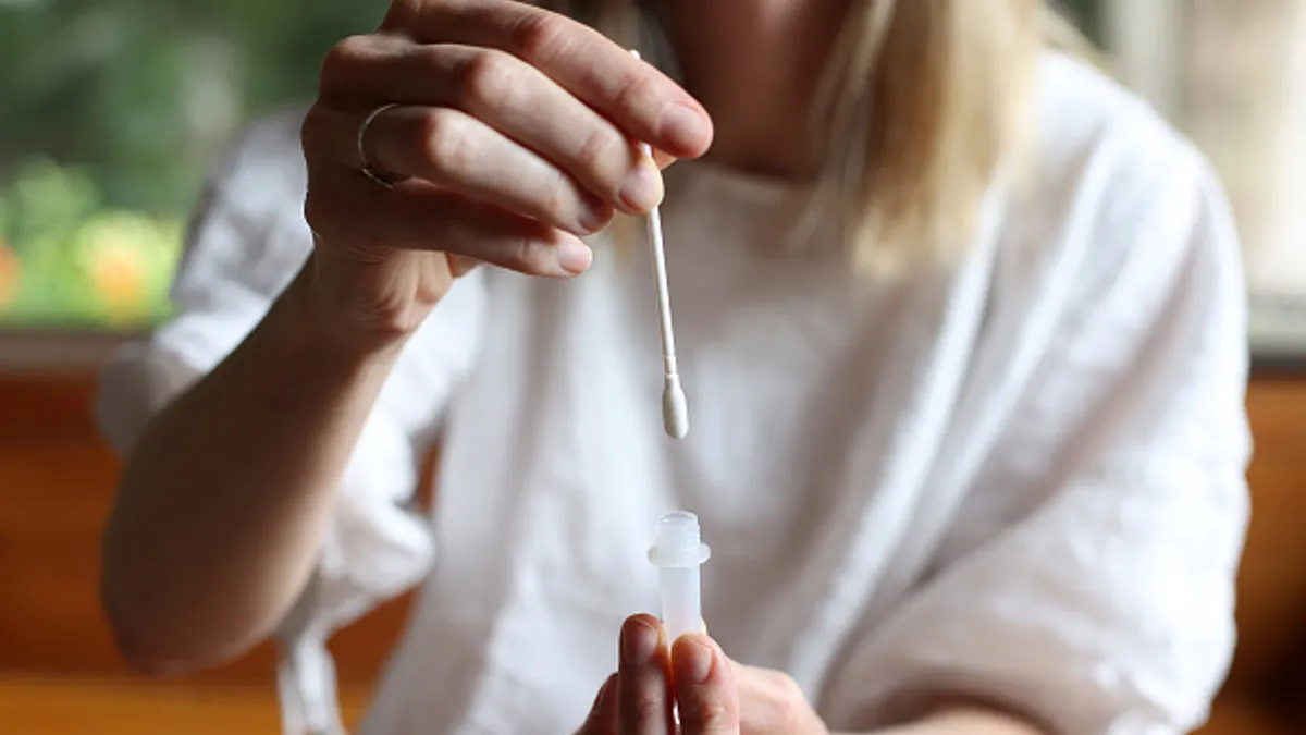 A person holds up a swab and a test tube for a rapid antigen test kit.