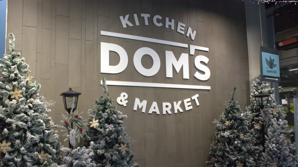 Sign that says Dom's Kitchen and Market surrounded by Christmas trees and string lights.