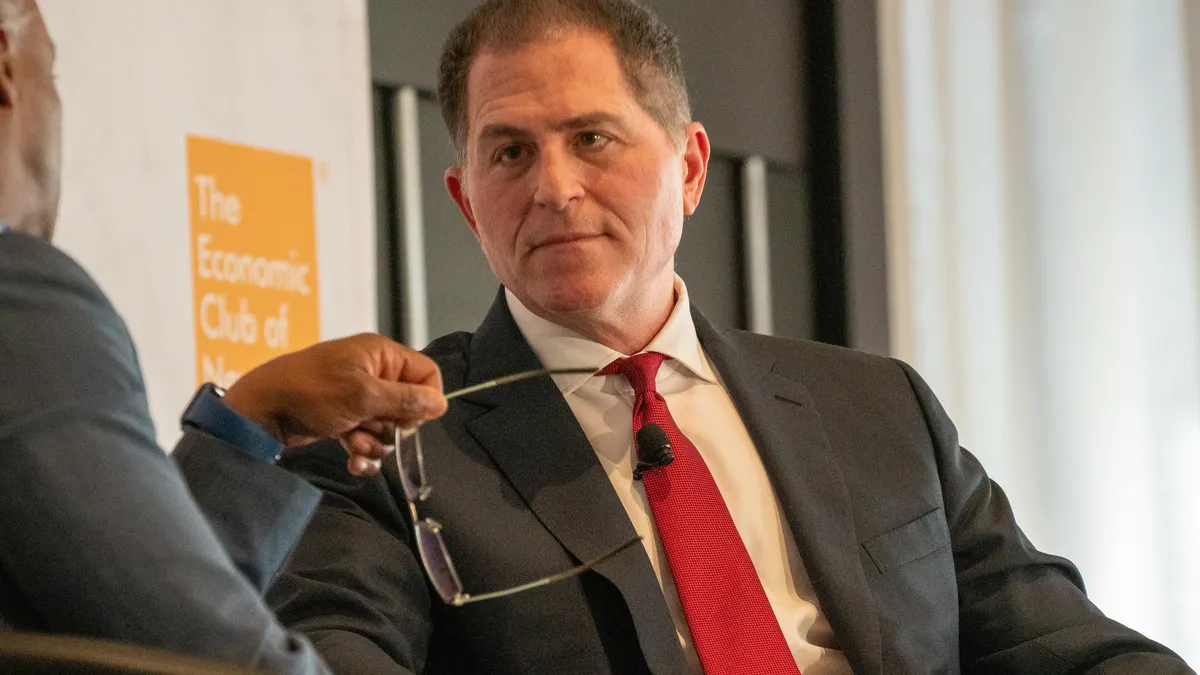 A person in a suit gestures with his hands while speaking.