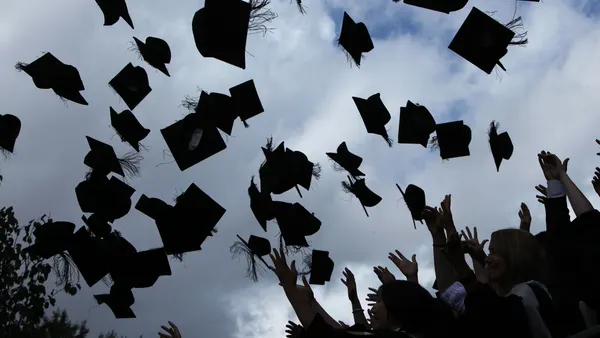 The silhouette of dozens of gowned students throwing their graduation mortarboards in the air is shown against a bright blue sky as they celebrate, a portend of the bright future that lay ahead.