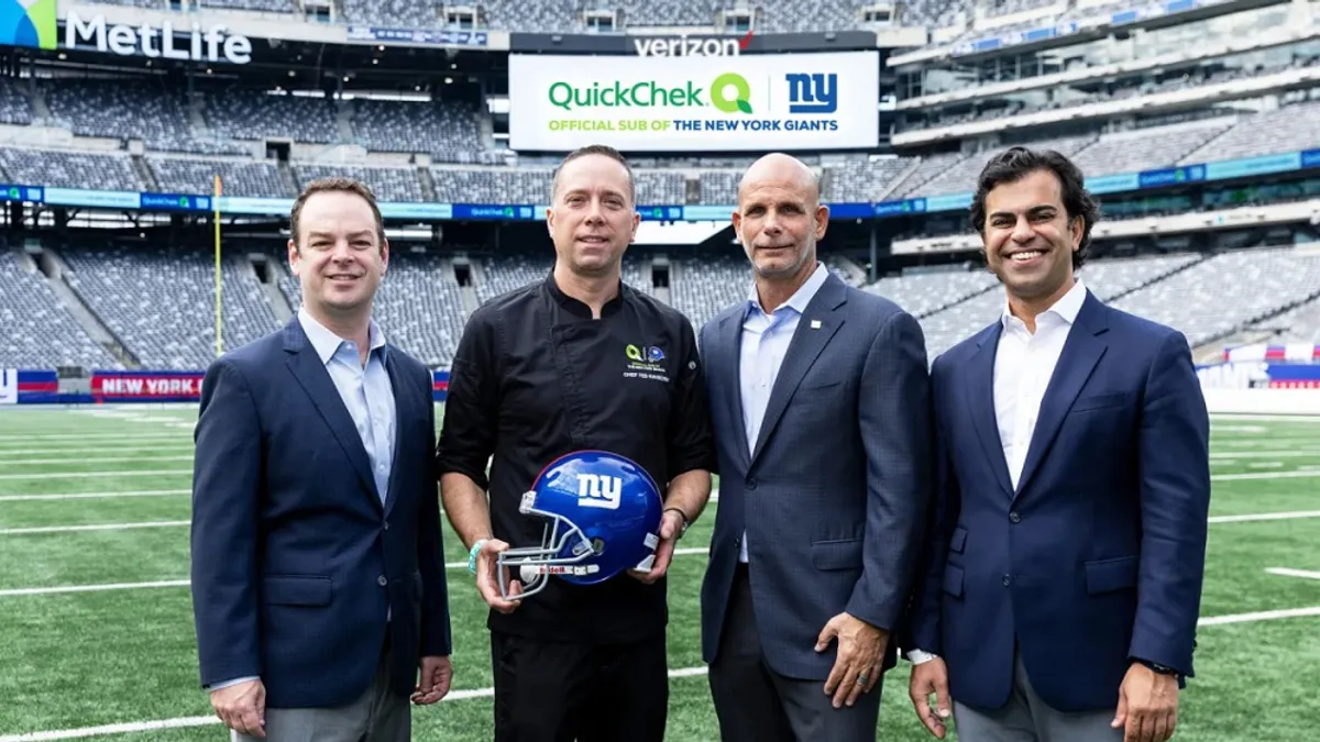 A photo of four men standing in MetLife Stadium, with one of them holding a New York Giants football helmet.