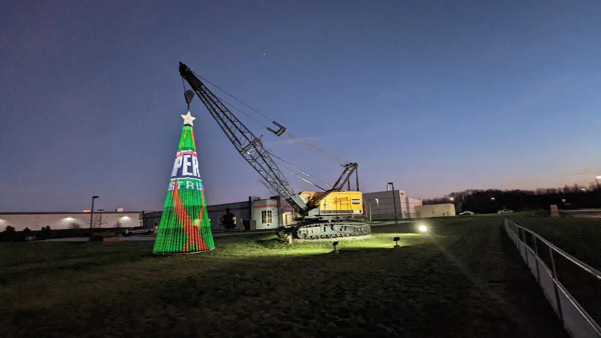 A large crane holds up a brightly lit metal "Christmas tree." The tree has the Superior Construction logo on it, and it's nighttime.