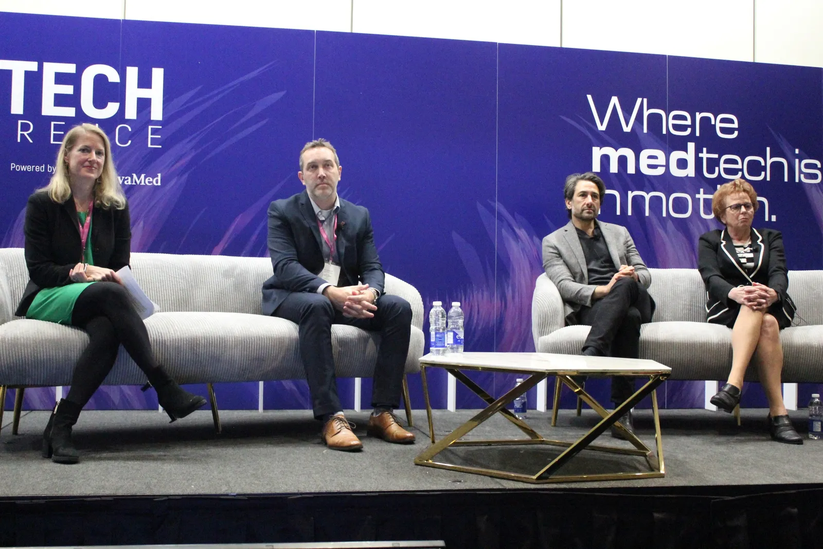 Four people sit on a stage on couches.