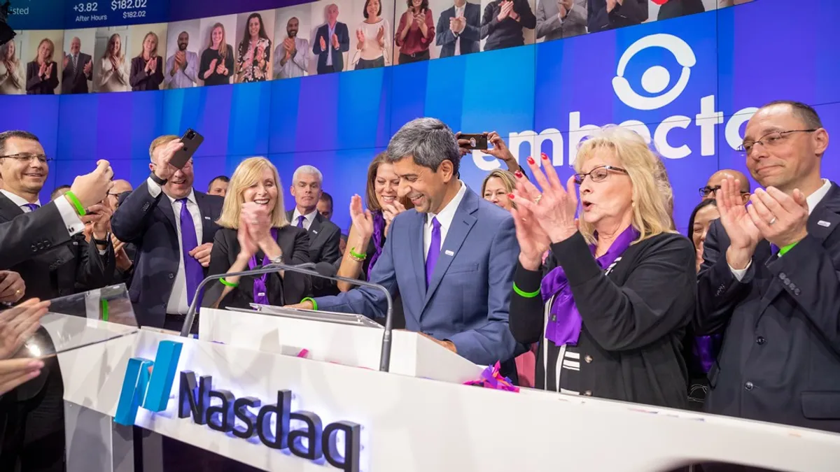 Embecta CEO Dev Kurdikar stands at a podium that says "Nasdaq" while people clap around him.