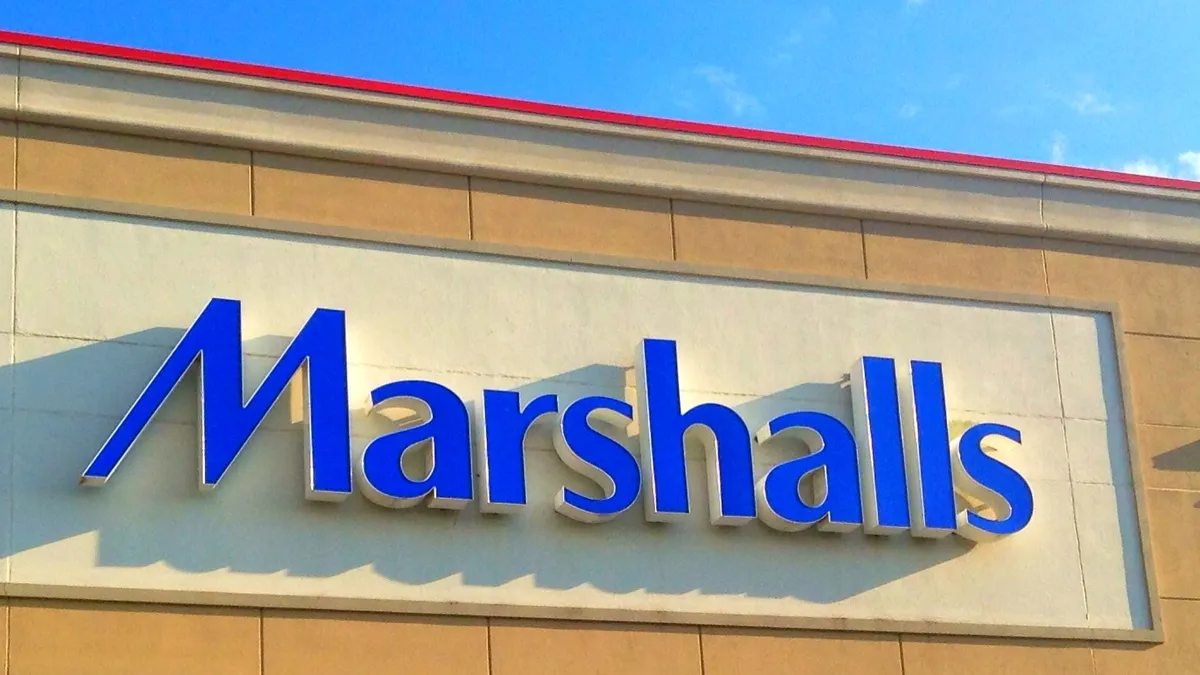 A sign with bright blue letters reads "Marshalls," on a building against a bright blue sky.