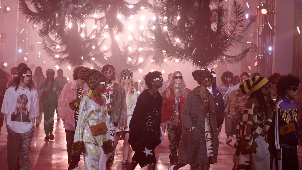 Models wear streetwear and walk on a darkened runway beneath upside down palm trees.