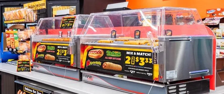 A photo of hot dogs on a roller grill inside a convenience store. The from of the grill has a Nathan&#x27;s logo and says &quot;mix and match 2 for $3.33&quot;