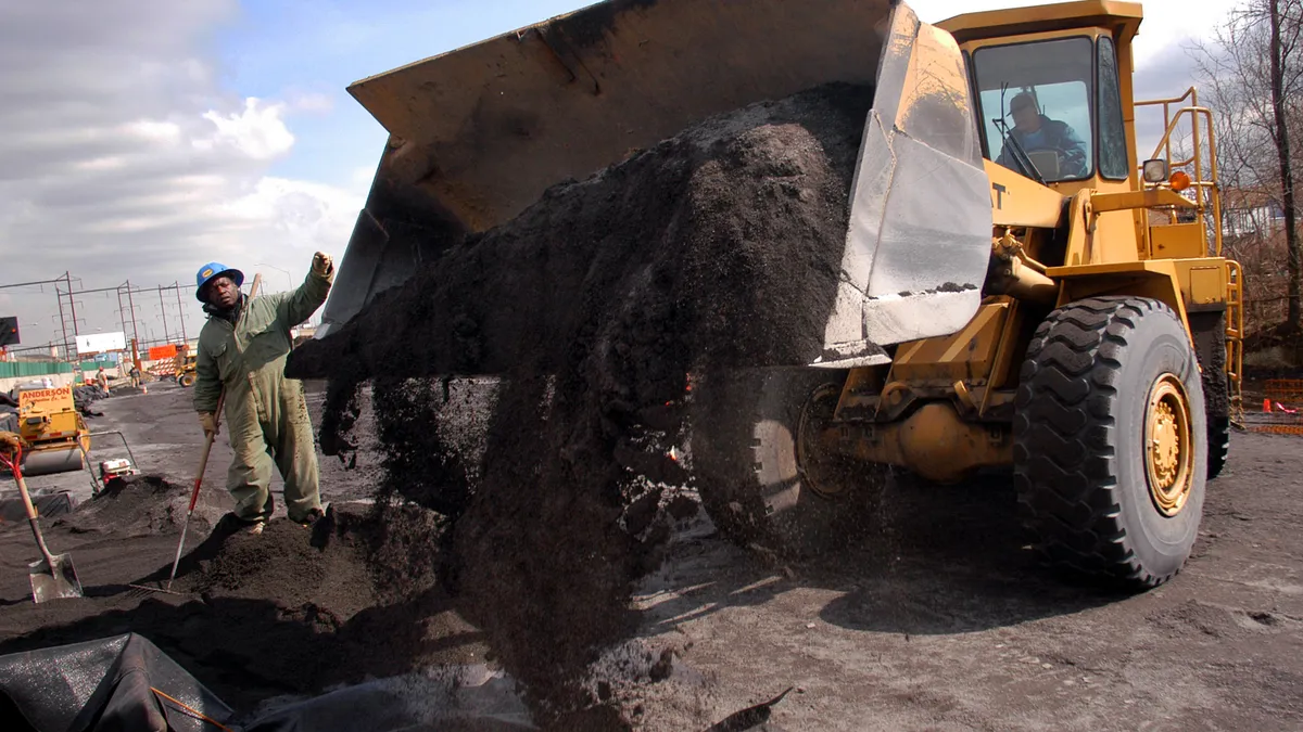 A construction worker directs a bulldozer loaded with pebbles that will serve as the base for a new highway.