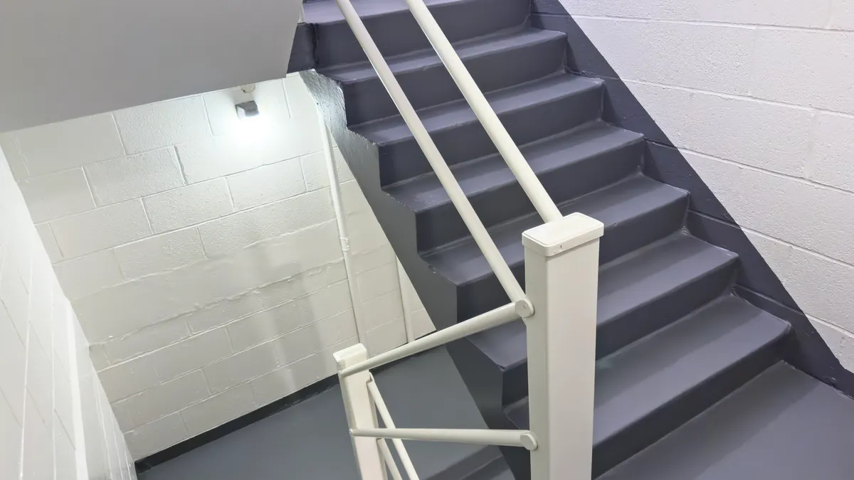 An interior gray staircase with a white metallic railing and white brick wall.