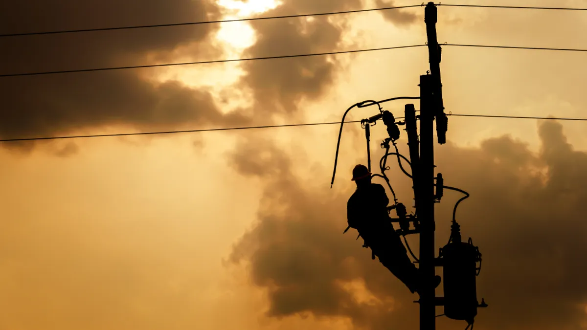 The silhouette of a power line worker climbing on an electric pole replacing a damaged line.