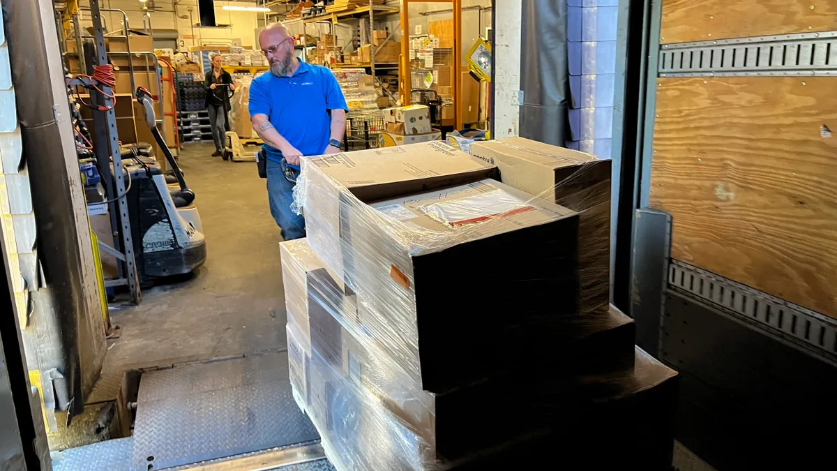 A person pulls a shipment out of the back of a trailer onto a loading dock.