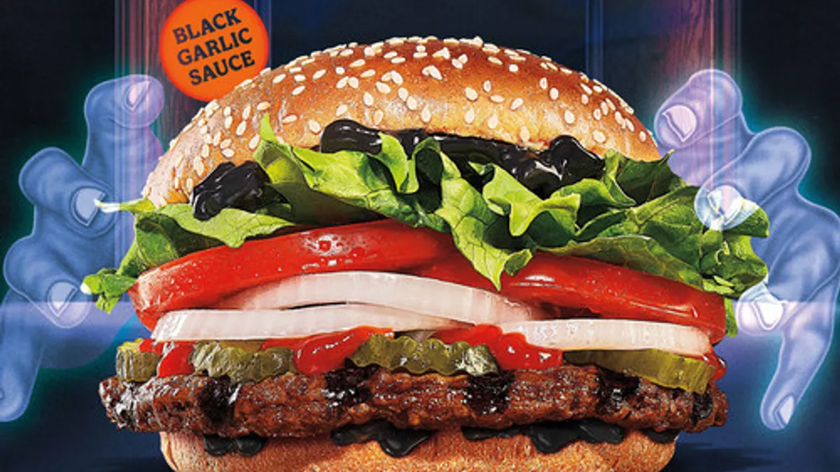 A pair of ghostly hands surround a new Burger King Whopper that features black sauce underneath orange text reading, "Home of the Ghosts Whopper."