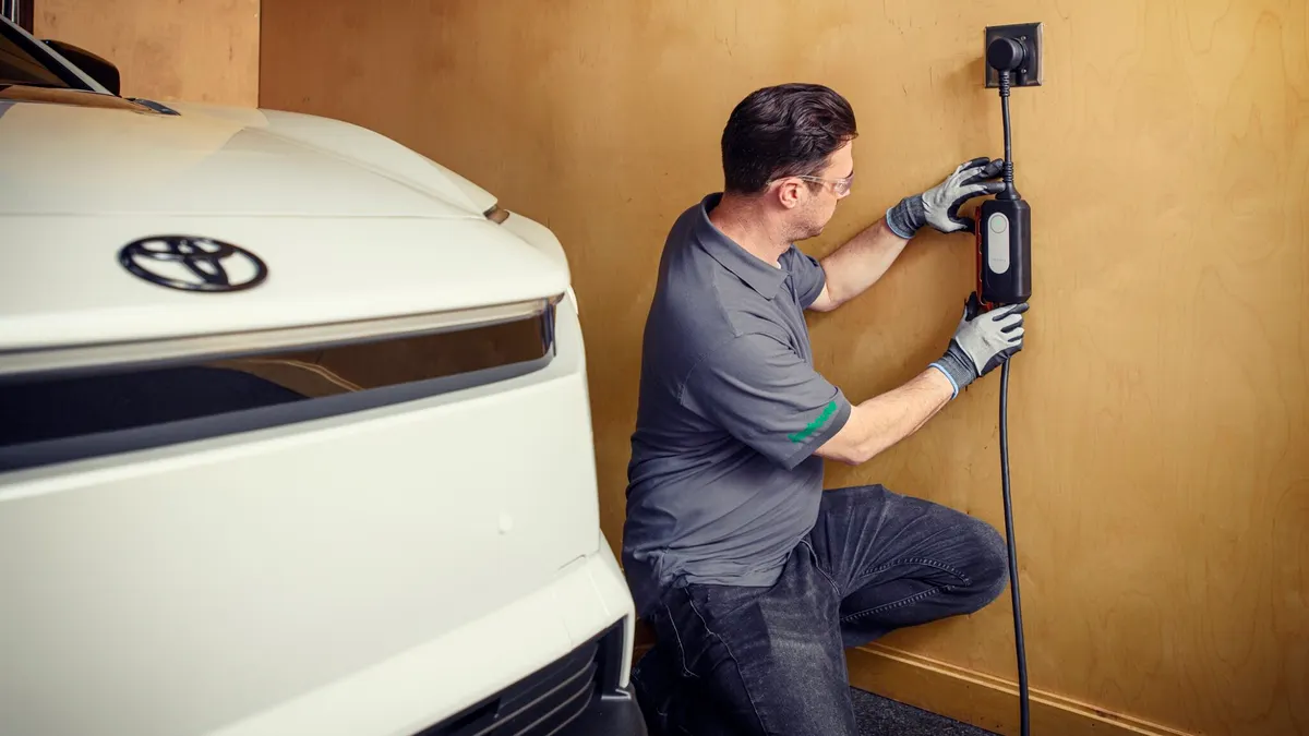 An electrician installing a residential EV charger on a wall next to a while Toyota vehicle showing the company's logo.