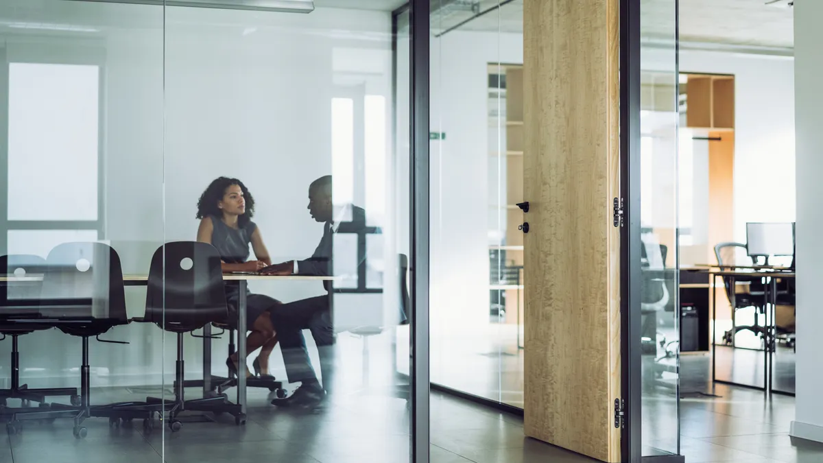 Two people talk in a conference room.