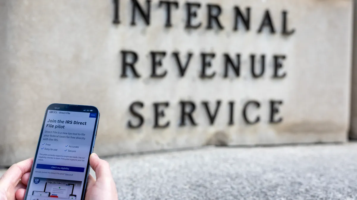 A person holds a smart phone on the IRS Direct File page in front of the Internal Revenue Service Building.