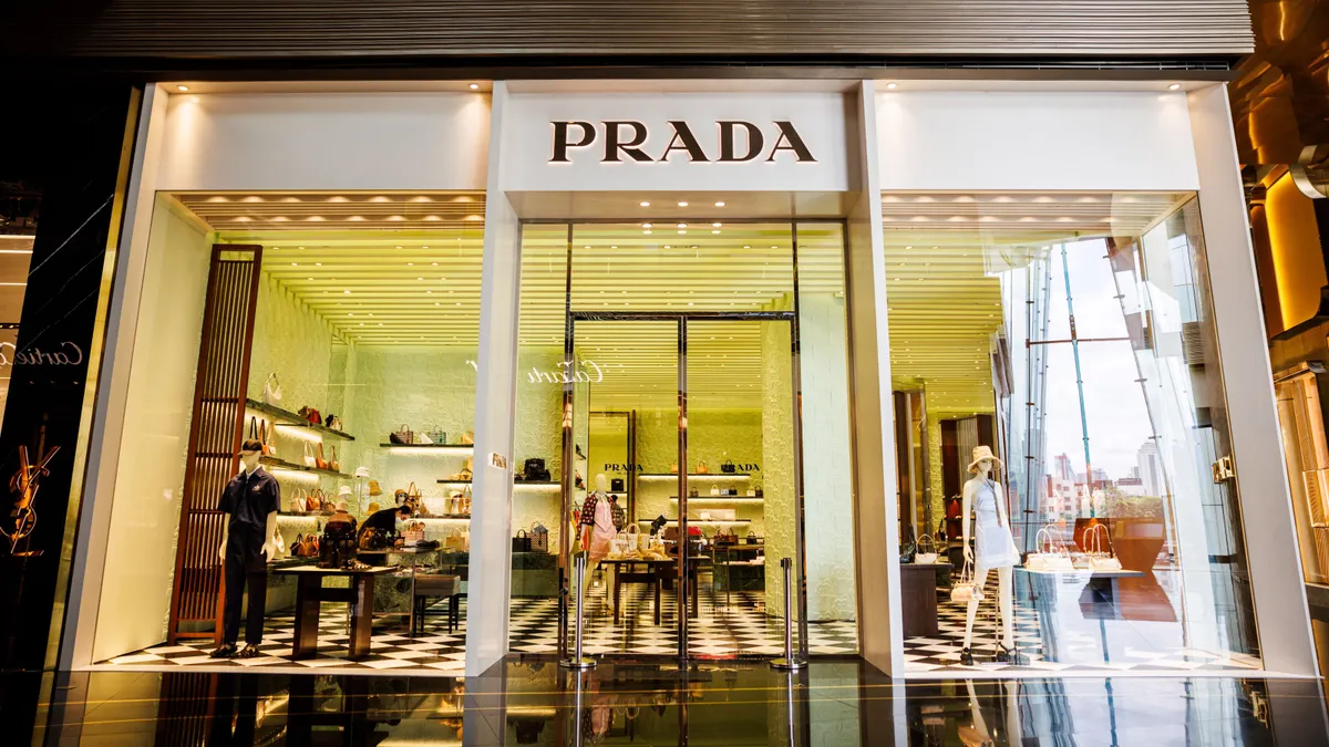 A storefront with the word Prada written on the front is lit up within.