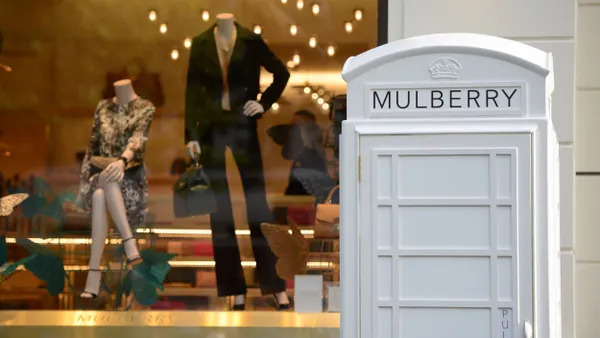 An exterior of a Mulberry store, with a fake telephone box outside of it. Two mannequins are in the window display.