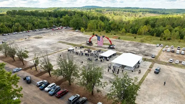 A skyshot of two cranes holding a large American flag while people gather on a large plot of dirt.
