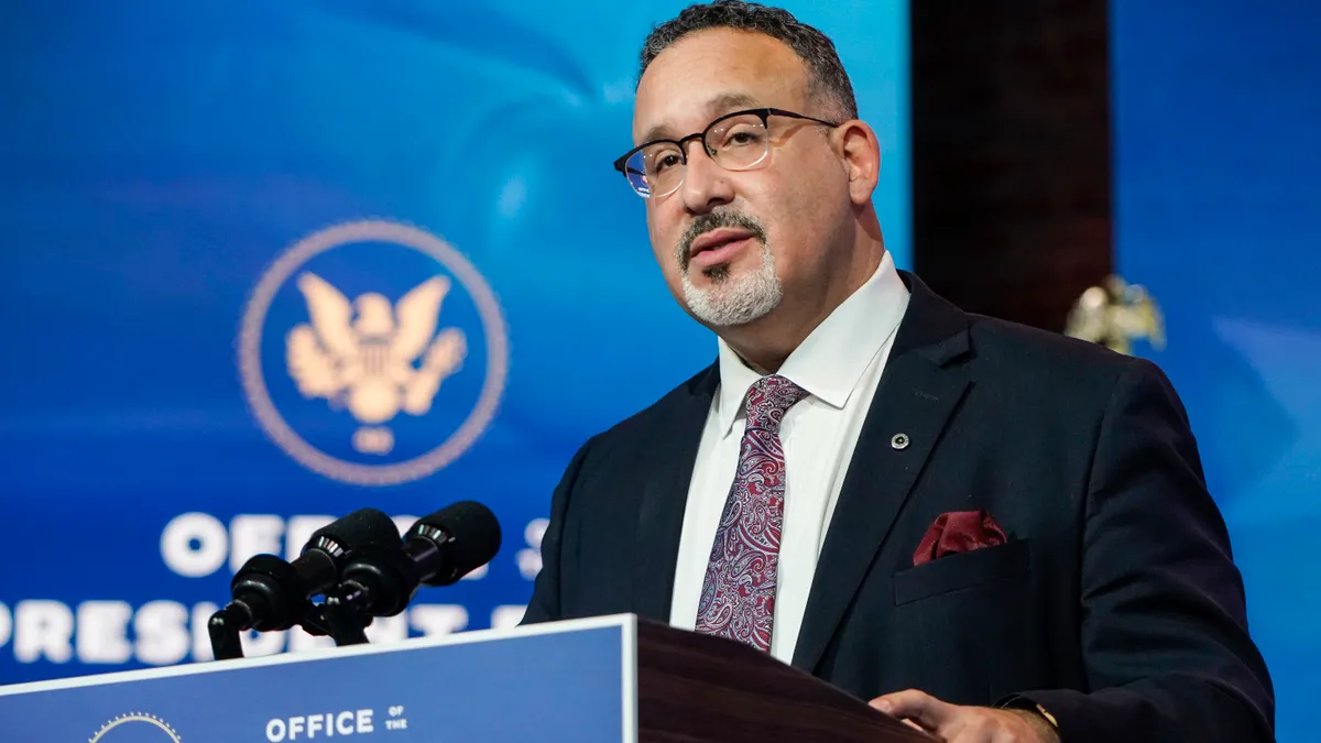 Miguel Cardona speaking at a podium.