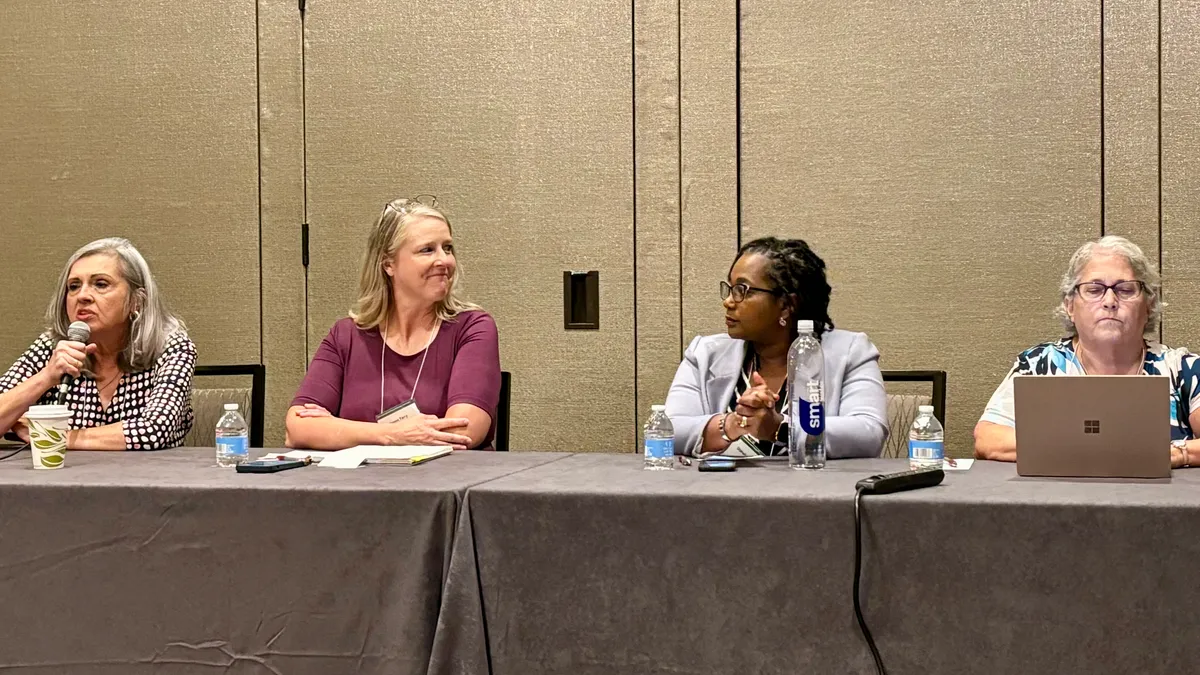 Four people are sitting at a table in a room. There is a microphone and laptop on the table