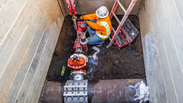 Person wearing a yellow uniform working underground on pipes.