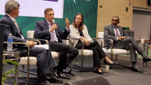 Four people sit on a stage. One of them holds a microphone and talks.