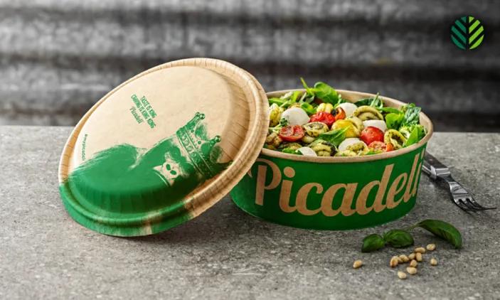 A brown fiber-based bowl lid with green printing rests on a fiber-based bowl with salad inside.