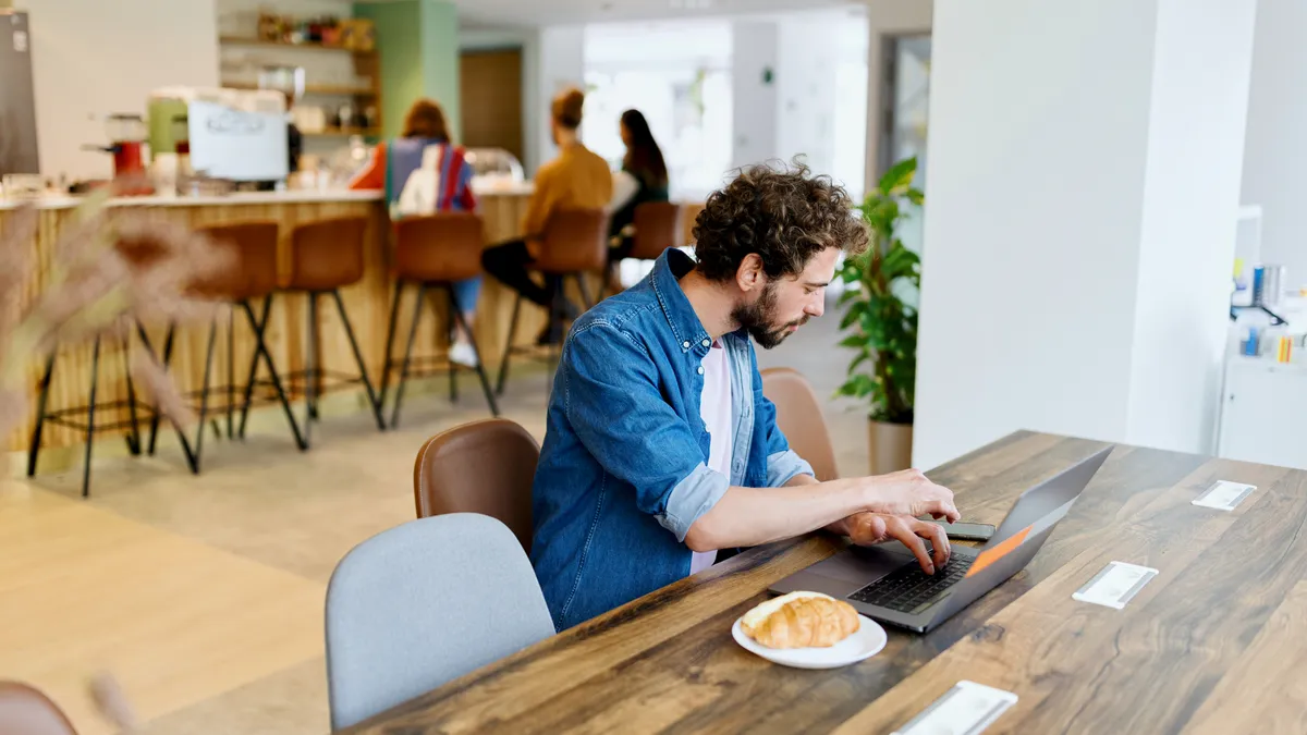 An employee works from a small desk in an office cafeteria.