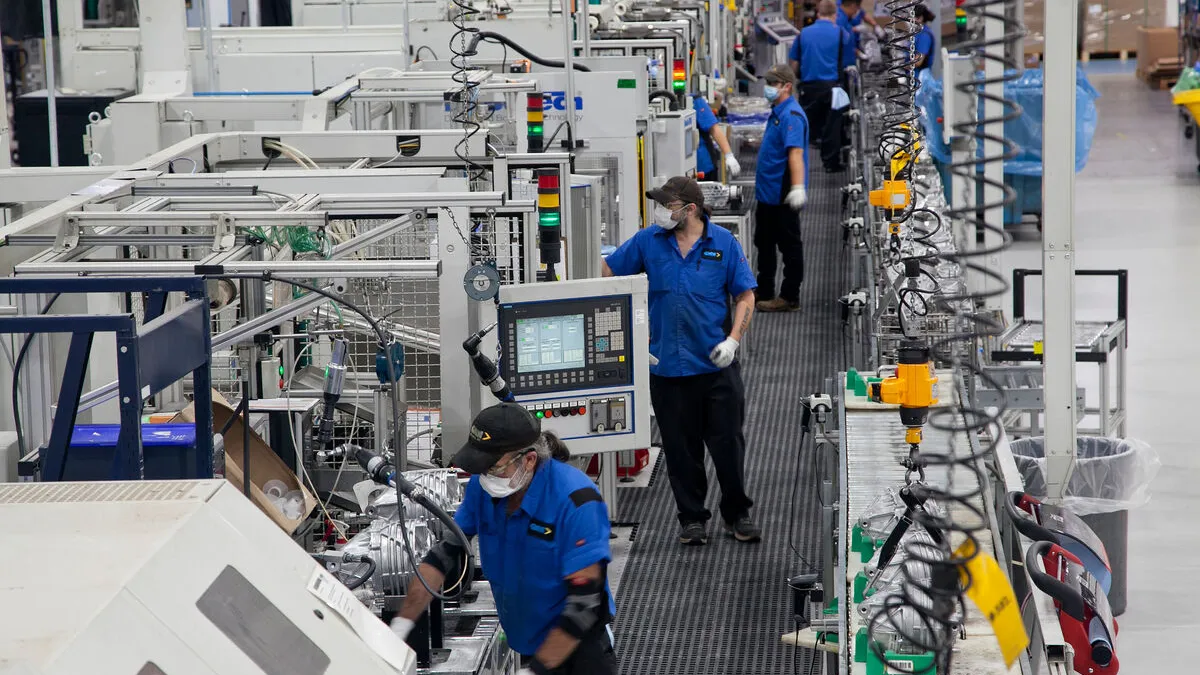 People in blue shirts and protective gear working in a factory line.