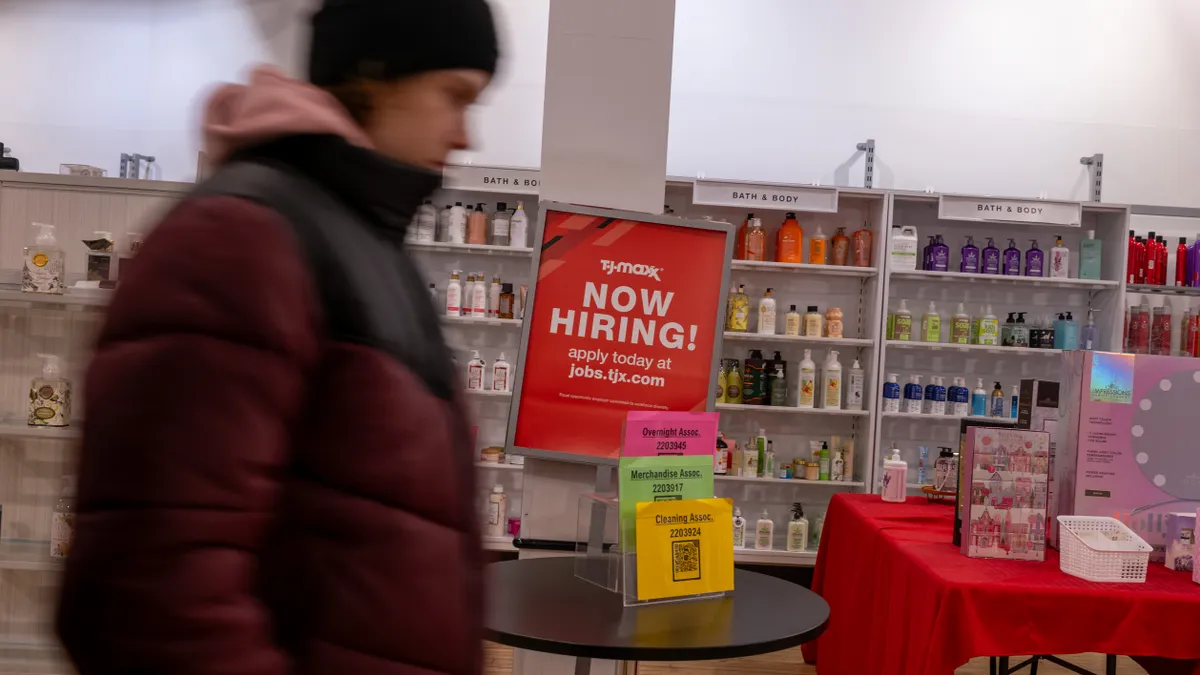 A person walks past a "now hiring" sign in a store.