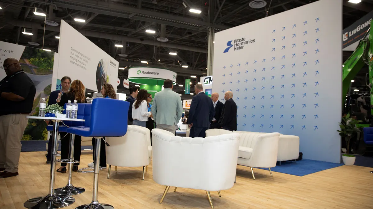 People stand around a promotional booth featuring material for Waste Harmonics Keter in an exposition hall.